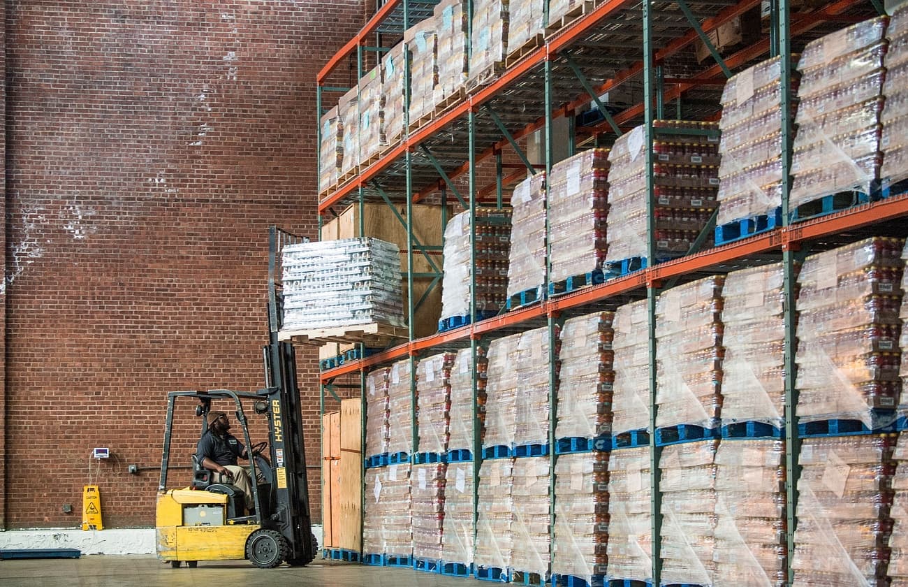Forklift operator moving palletized inventory inside a large warehouse operations space