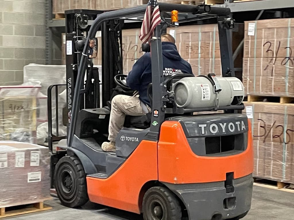 Forklift consolidating palletized equipment in a warehouse staging area